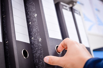 Close up on hand holding multicolored office folders on the bookshelf backgrounds. Many working stationery, stacked records. Different color spectrum. Educational or financial file-box object supplies