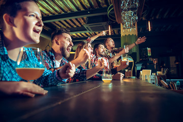 Sport, people, leisure, friendship and entertainment concept - happy football fans or male friends drinking beer and celebrating victory at bar or pub