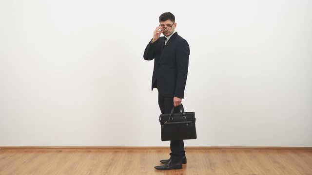 The businessman in glasses walking with a bag on the white wall background