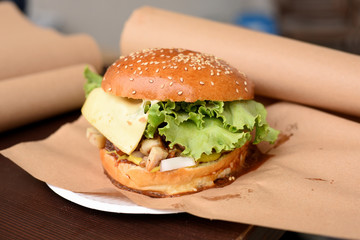 tasty grilled beef burger with lettuce and cheese served on pieces of brown paper on wooden table, street food