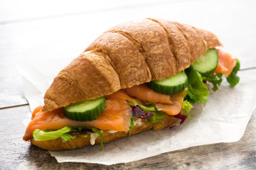 Croissant sandwich with salmon and vegetables on wooden table.