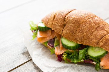 Croissant sandwich with salmon and vegetables on wooden table.