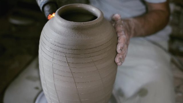 Closeup potter warm up glazes along all clay jar by hair dryer on potter's wheel