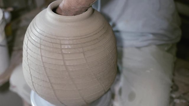 Closeup potter stretches jar by hand on potter's wheel