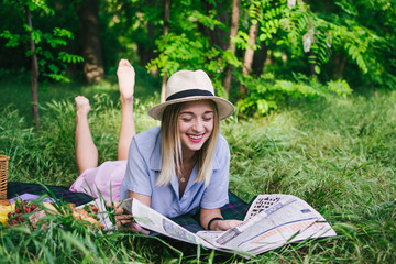 Portrait of happy romantic young woman in hat reading magazine outdoors in park on picnic