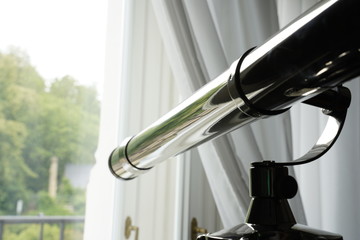 Beautiful old metallic telescope on a tripod watching out of the window