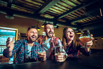 Sport, people, leisure, friendship and entertainment concept - happy football fans or male friends drinking beer and celebrating victory at bar or pub