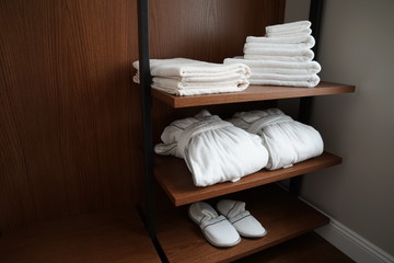Folded towels, carpet slippers and bathrobes on a shelf of a closet in a hotel
