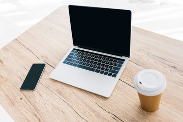 closeup view of smartphone with blank screen, laptop and coffee cup on wooden table