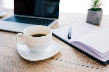 close up view of coffee cup, empty textbook and laptop with blank screen on wooden table