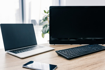 closeup view of smartphone with blank screen, laptop and computer at wooden table