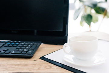 closeup view of cup of coffee on empty clipboard and computer at wooden table
