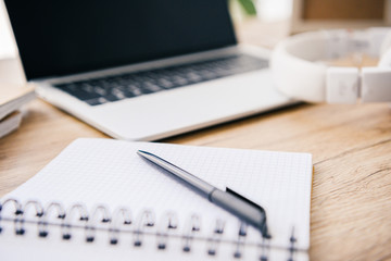 close up view of empty textbook with pen at table with laptop and headphones