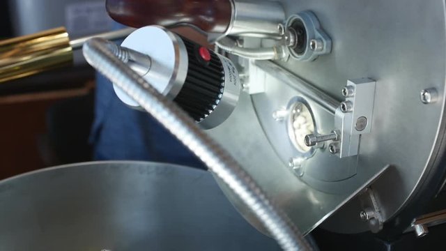 Professional coffeemachine and raw coffee beans. White coffee beans are fried in a professional machine for coffee beans to make real coffee. Slow motion.