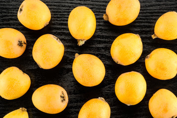 Fresh orange Japanese loquats flatlay isolated on black wood background.