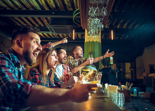 Sport, people, leisure, friendship and entertainment concept - happy football fans or male friends drinking beer and celebrating victory at bar or pub