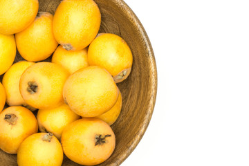 Fresh orange Japanese loquats in a wooden bowl flatlay isolated on white background.