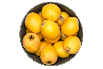 Fresh orange Japanese loquats in a grey ceramic bowl flatlay isolated on white background.