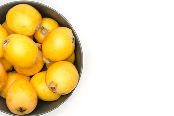 Fresh orange Japanese loquats in a grey ceramic bowl top view isolated on white background.