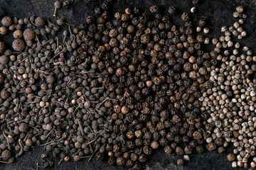 Variety of different black peppers allspice, pimento, monks pepper, peppercorns over old black iron texture surface. Food background. Top view, space.