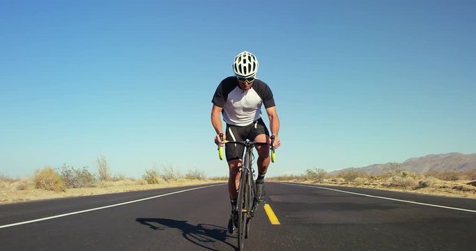 Slow motion young healthy man cycling on road bike outside on desert road on sunny day with blue sky in background 