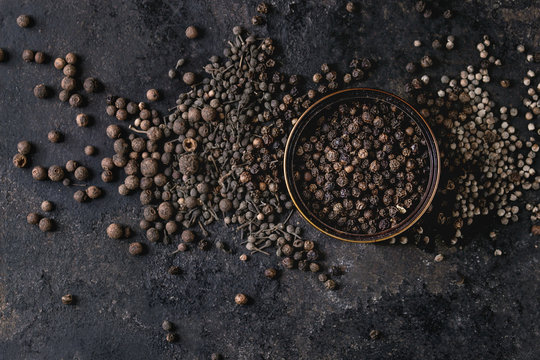 Variety of different black peppers allspice, pimento, monks pepper, peppercorns and ground powder in tin can over old black iron texture background. Top view, space.