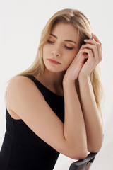 Young beautiful sexy woman in blue jeans shorts and black shirt posing and sitting on simple black chait in white studio. Fashion model with long straight hair and closed eyes.