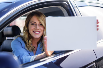 Woman sitting in the car and holding a white blank poster.