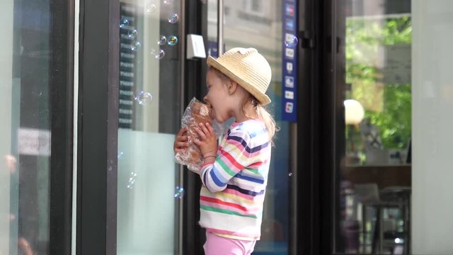 Little kid girl eating a tasty sweet baking pastry bun staying on a street during walking in city