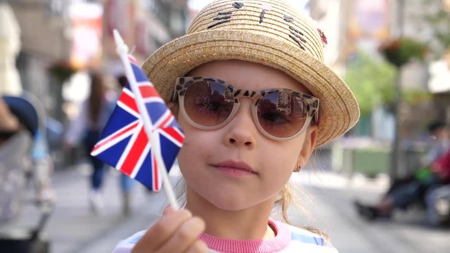 Little cute child girl portrait stay in city holding a flaf of United Kingdom of Great Britain