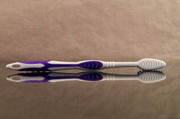 A toothbrush made of plastic with purple insets on the handle, laid on its side with reflection in...