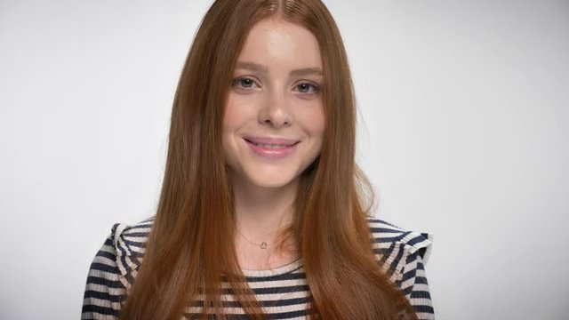 Portrait of a cute gignger girl looking at the camera smiling, white background