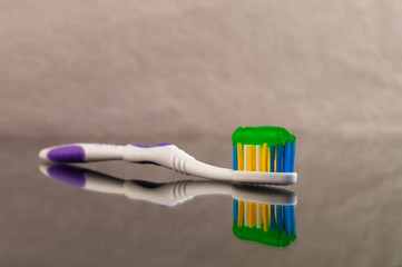 One toothbrush with toothpaste green on a gray abstract background with reflection.