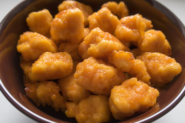 Appetizing and tasty fried pieces of chicken in a batter located in a deep plate on a light background close-up