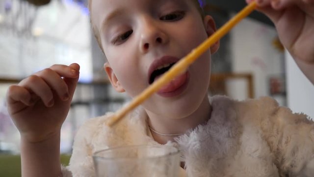Cute little girl in cafe with milkshake cocktail lick a cream foam from straw