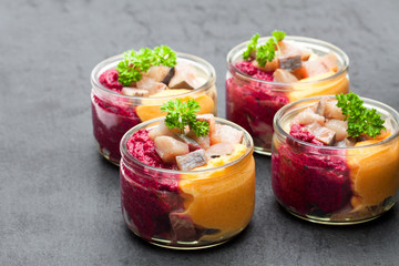 Herring  salad with colorful vegetables in a small glass jars on black stone background