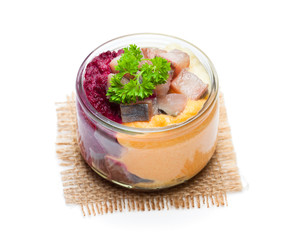 Herring  salad with colorful vegetables in a small glass jar isolated on white
