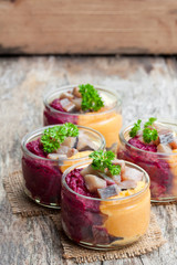 Herring  salad with colorful vegetables in a small glass jars on wooden table