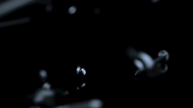 Steel nails falling over black background. Slow motion.
