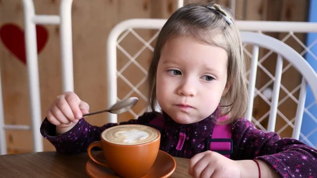 Little kid girl portrait eat a foam from cappuccino latte art with a spoon