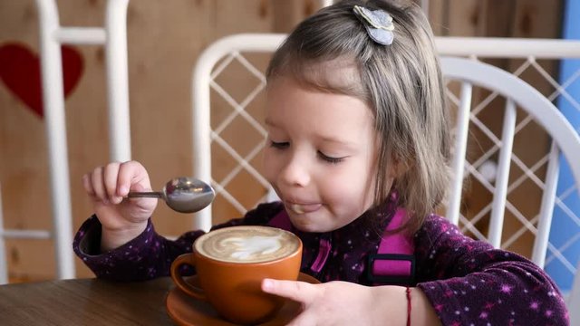 Little kid girl portrait eat a foam from cappuccino latte art funny lick with tongue