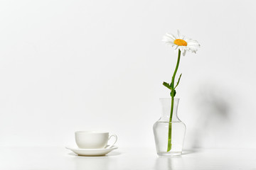 Naklejka na ściany i meble one chamomile flower and a cup in a vase on a table by the wall, white background