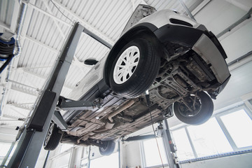 Car on a wheel alignment lift in auto service. Diagnosis of the chassis of the car raised at the elevator. - obrazy, fototapety, plakaty