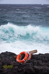 Obraz premium LANZAROTE, CANARY ISLANDS, SPAIN, EUROPE: Lifebouys on a rocky shoreline with waves crashing in the back.