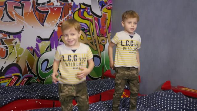 Little cute twin kids boys have fun play jump on a bed at home