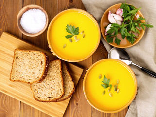 Two brown bowl of pumpkin soup with parsley and pumpkin seeds on brown dark wooden background, top view