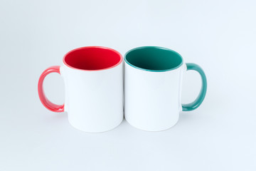 Two white mugs, with a green and red handle on a light background. 