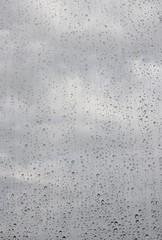 Raindrops on transparent window with cloudy sky background, closeup, copyspace