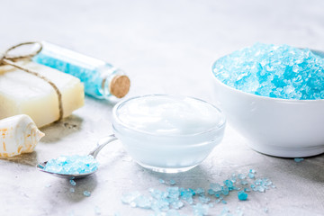 Fototapeta na wymiar blue bath salt, body cream and shells for spa on gray table back