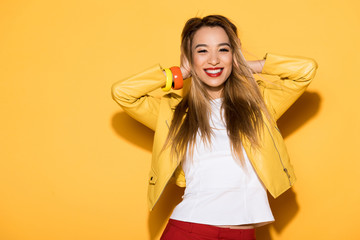 smiling asian female model closing ears by hands on yellow background